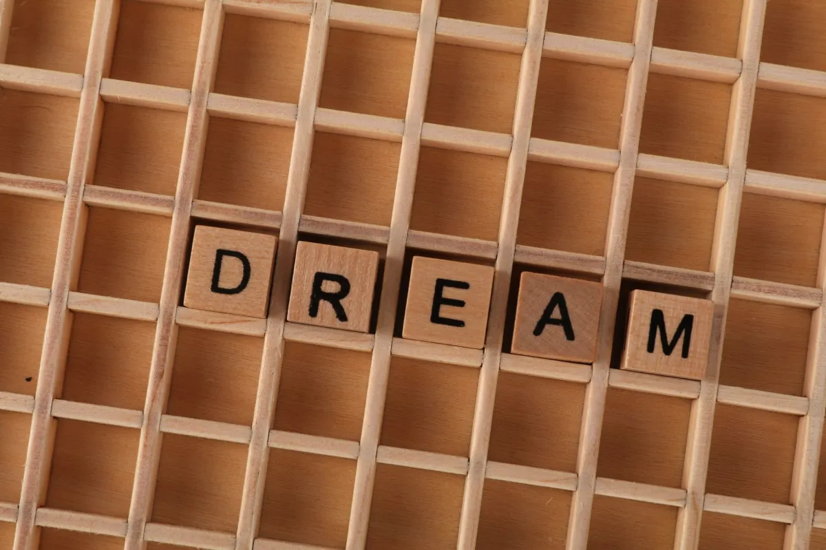 Wooden letter tiles spelling 'DREAM' on a grid background symbolizing aspirations.