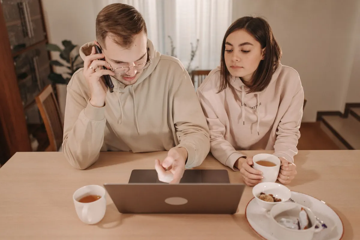 A couple enjoying coffee and online shopping together at home, using a laptop and smartphone.