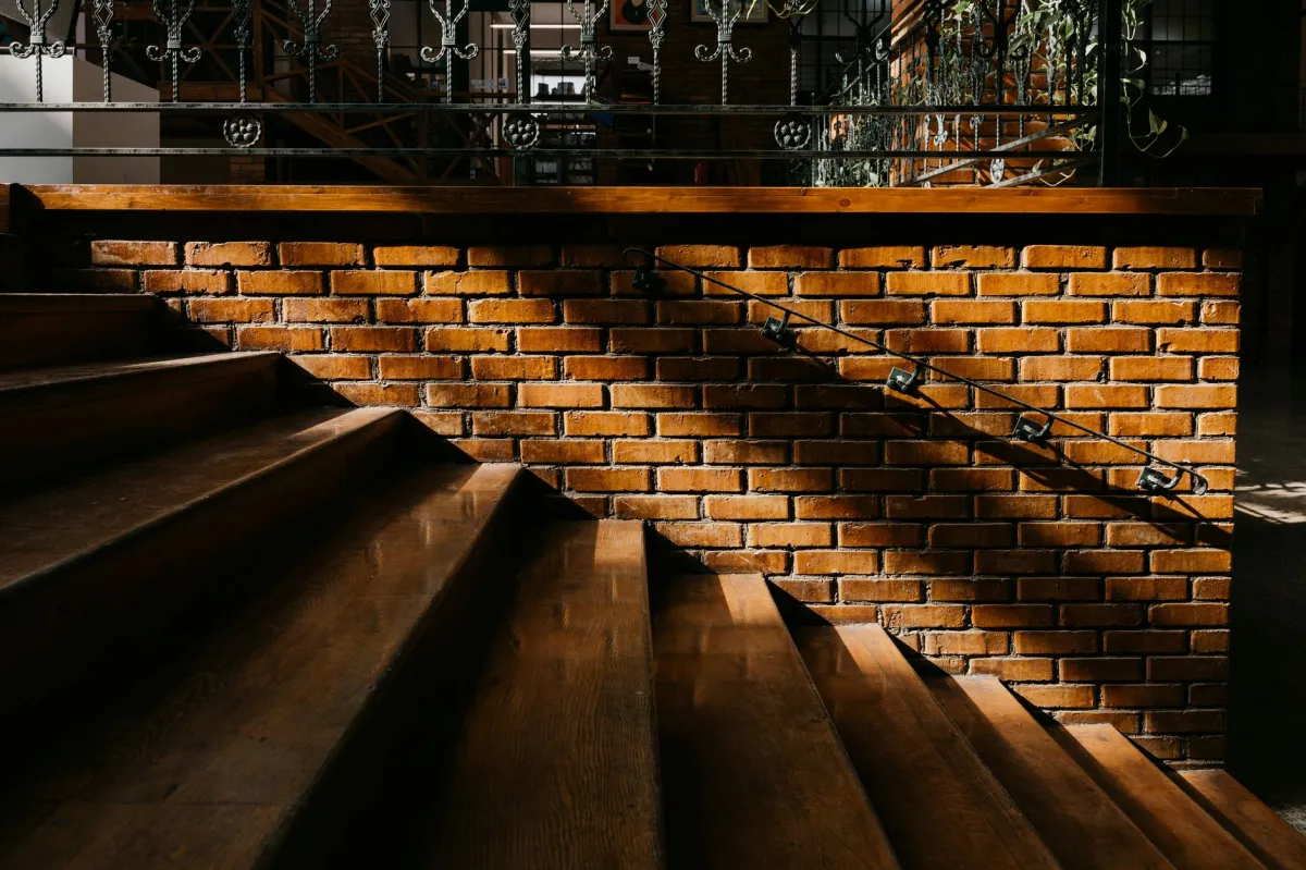 Sunlight casts shadows on a rustic brick staircase with iron railing in Baku.