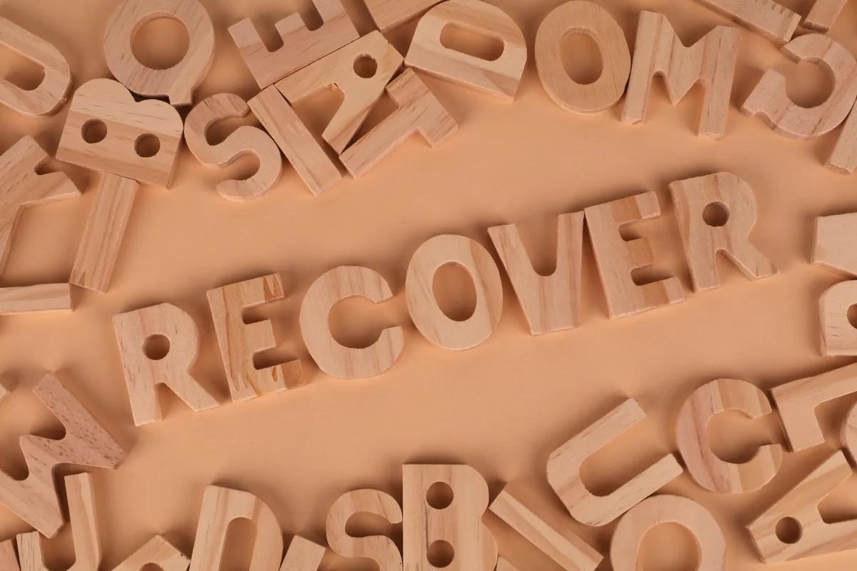 Flat lay of wooden alphabet letters with 'recover' highlighted.