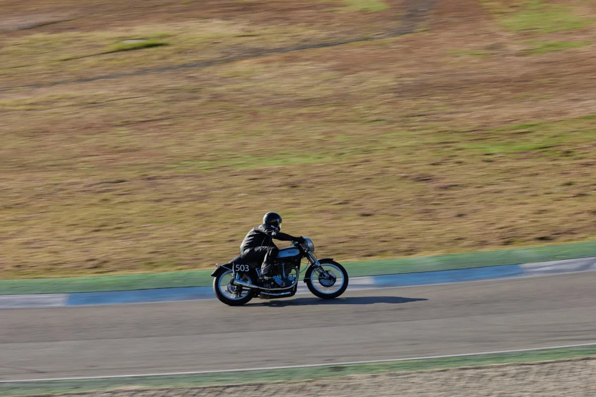 Motorcyclist on vintage bike racing on track during the day.