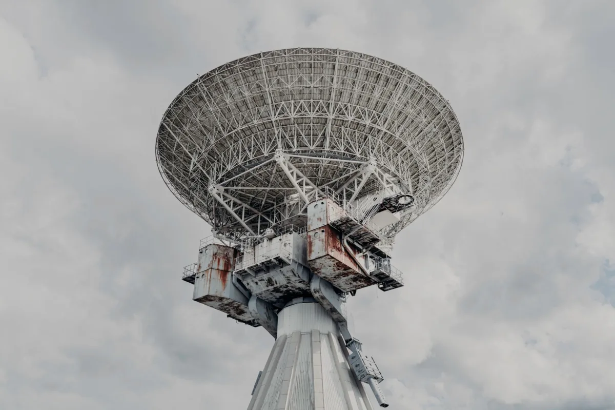 A large radio telescope under a cloudy sky, illustrating ground‑based support for satellite observations.