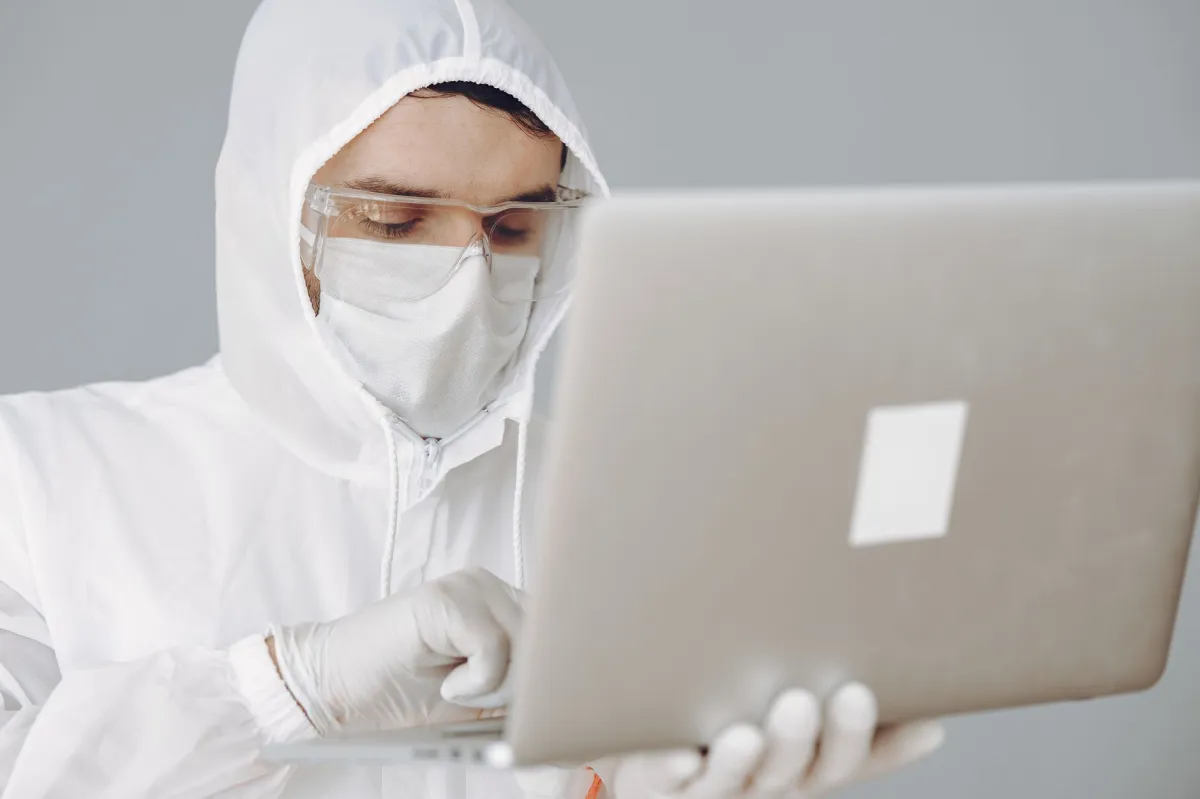 A healthcare worker in PPE using a laptop for remote work, symbolizing modern medicine and digital innovation.
